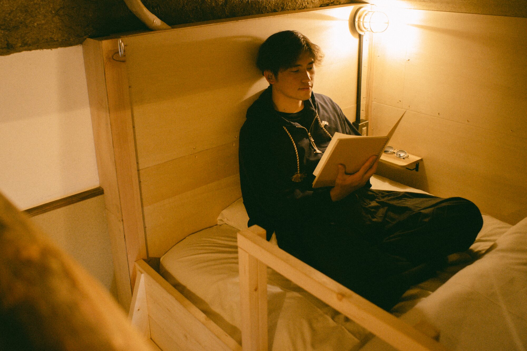 やわらかな照明のベッドスペースで読書をしてくつろぐ様子